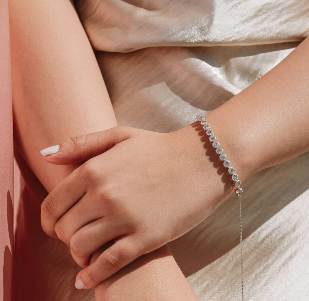 Close-up of manicured hands with pearl rings and bracelet on satin fabric.